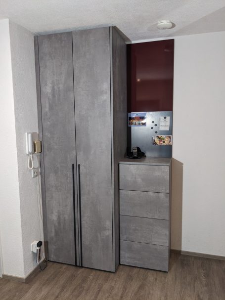 Graue Garderobenmöbel in Betonoptik mit Schrank, Schubladen und rote Rückwand. 